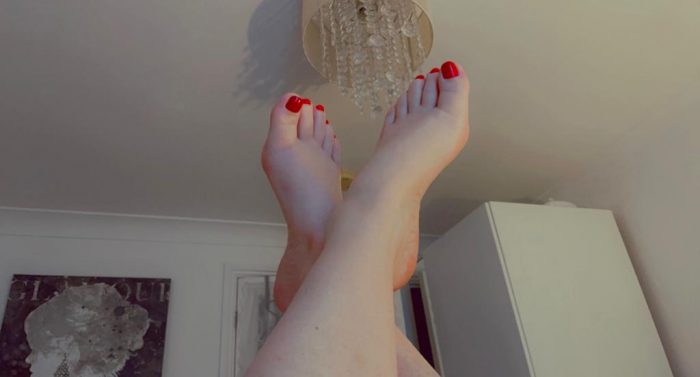 Red toenails on pale perfect feet poised in the air
